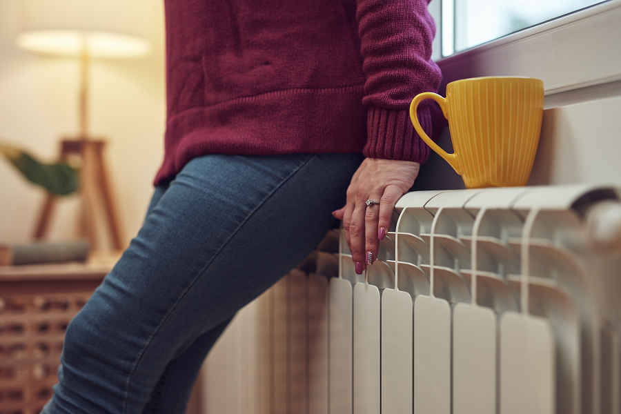 A woman leans against a radiator at home, beside a hot mug of tea.